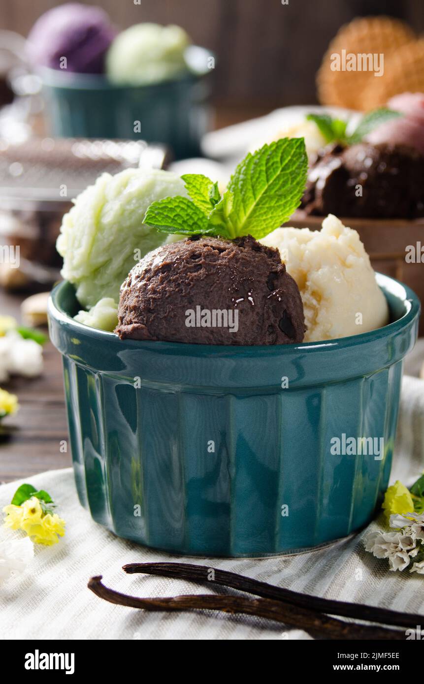 Three scoops of Vanilla pistachio and chocolate icecream balls in clay bowls on wooden kitchen table Stock Photo