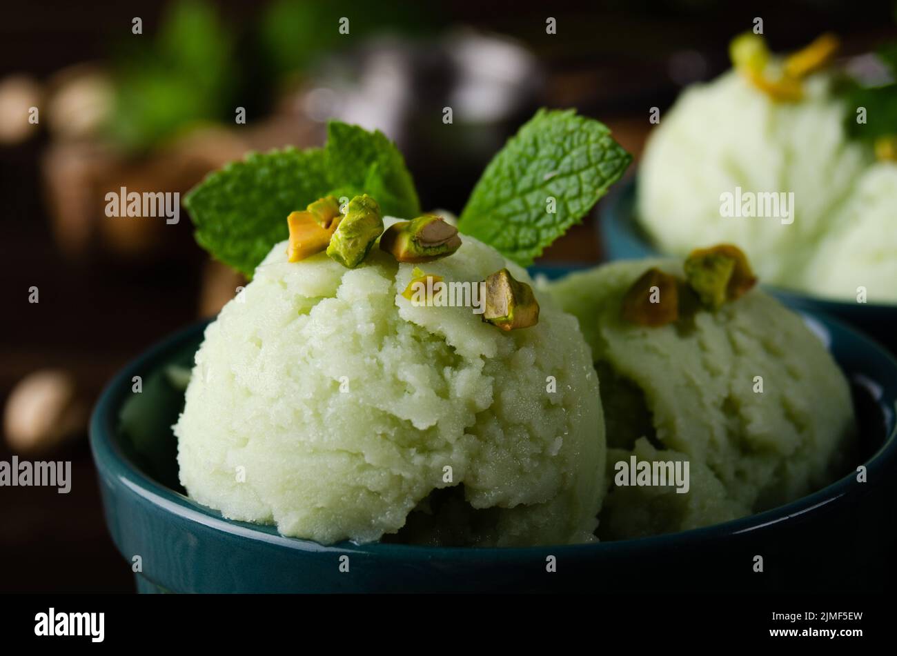 Pistachio icecream balls in clay bowls on wooden kitchen table with crumbs and nuts aside Stock Photo