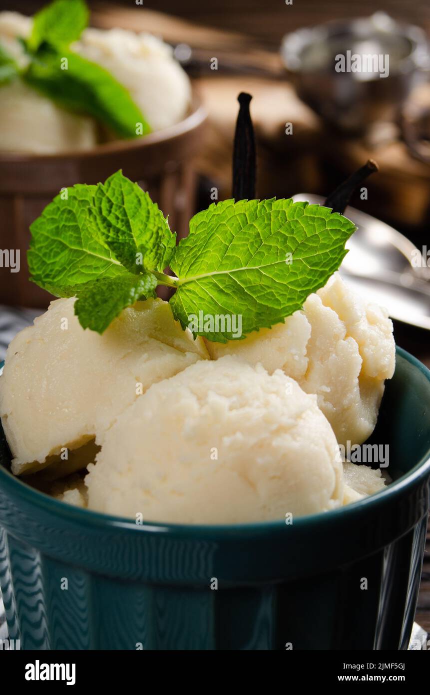Vanilla icecream balls in clay bowls on wooden kitchen table with ice cream scoop aside Stock Photo