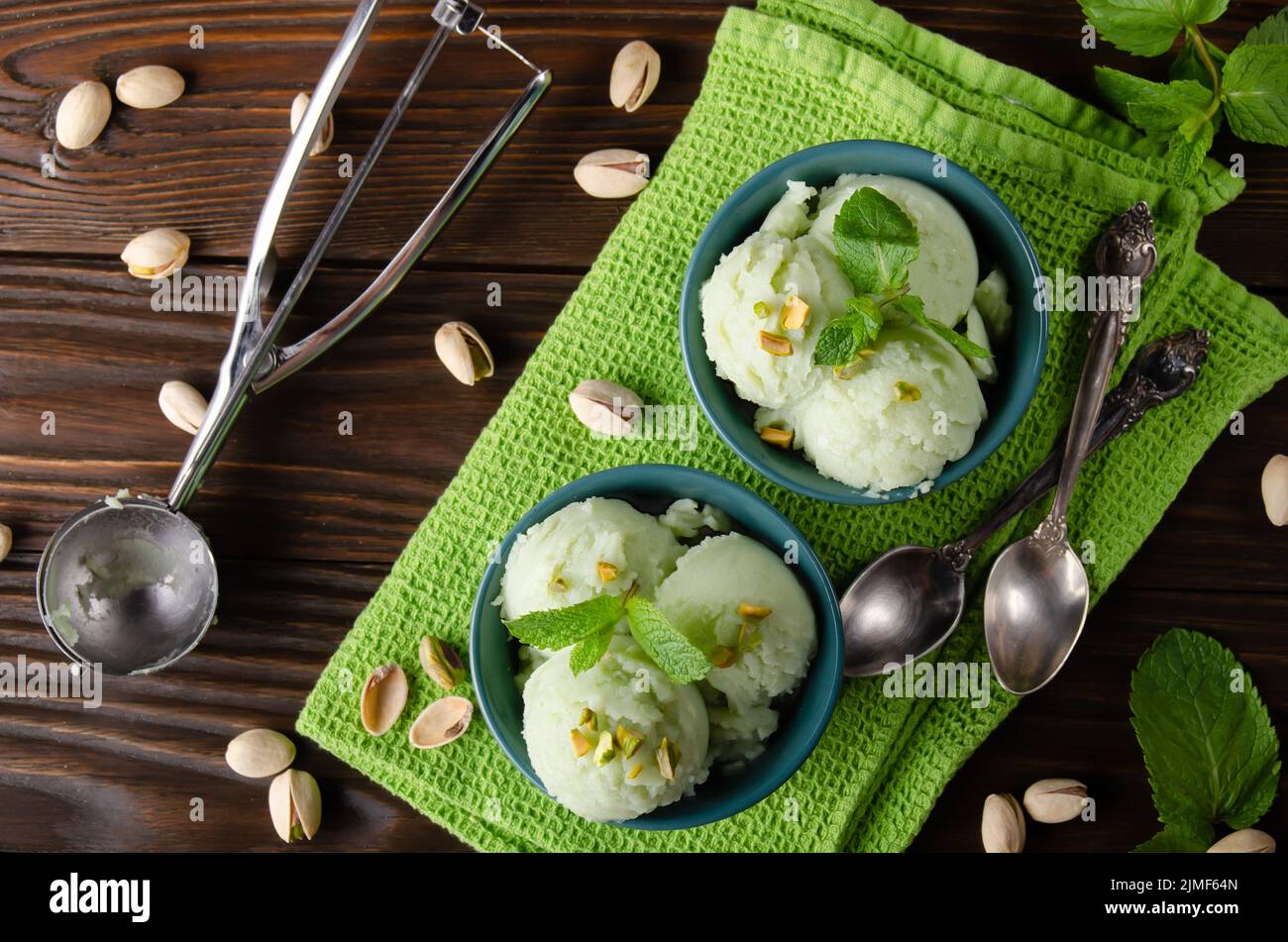 Pistachio icecream balls in clay bowls flat layed on wooden kitchen table with crumbs and nuts aside Stock Photo