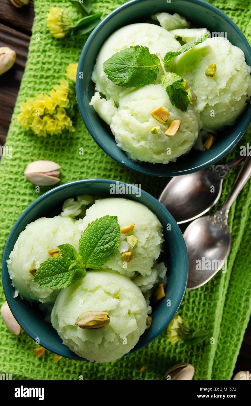 Pistachio icecream balls in clay bowls flat layed on wooden kitchen table with crumbs and nuts aside Stock Photo