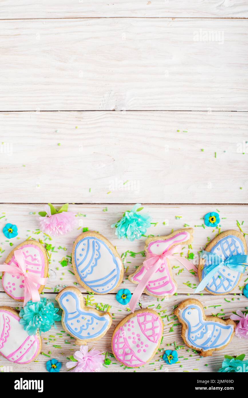 Sugar sprinkles and Easter frosted cookies in shape of egg chicken and rabbit on white wooden table background. Flat lay vertica Stock Photo