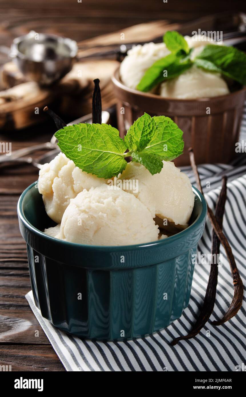 Vanilla icecream balls in clay bowls on wooden kitchen table with ice cream scoop aside Stock Photo
