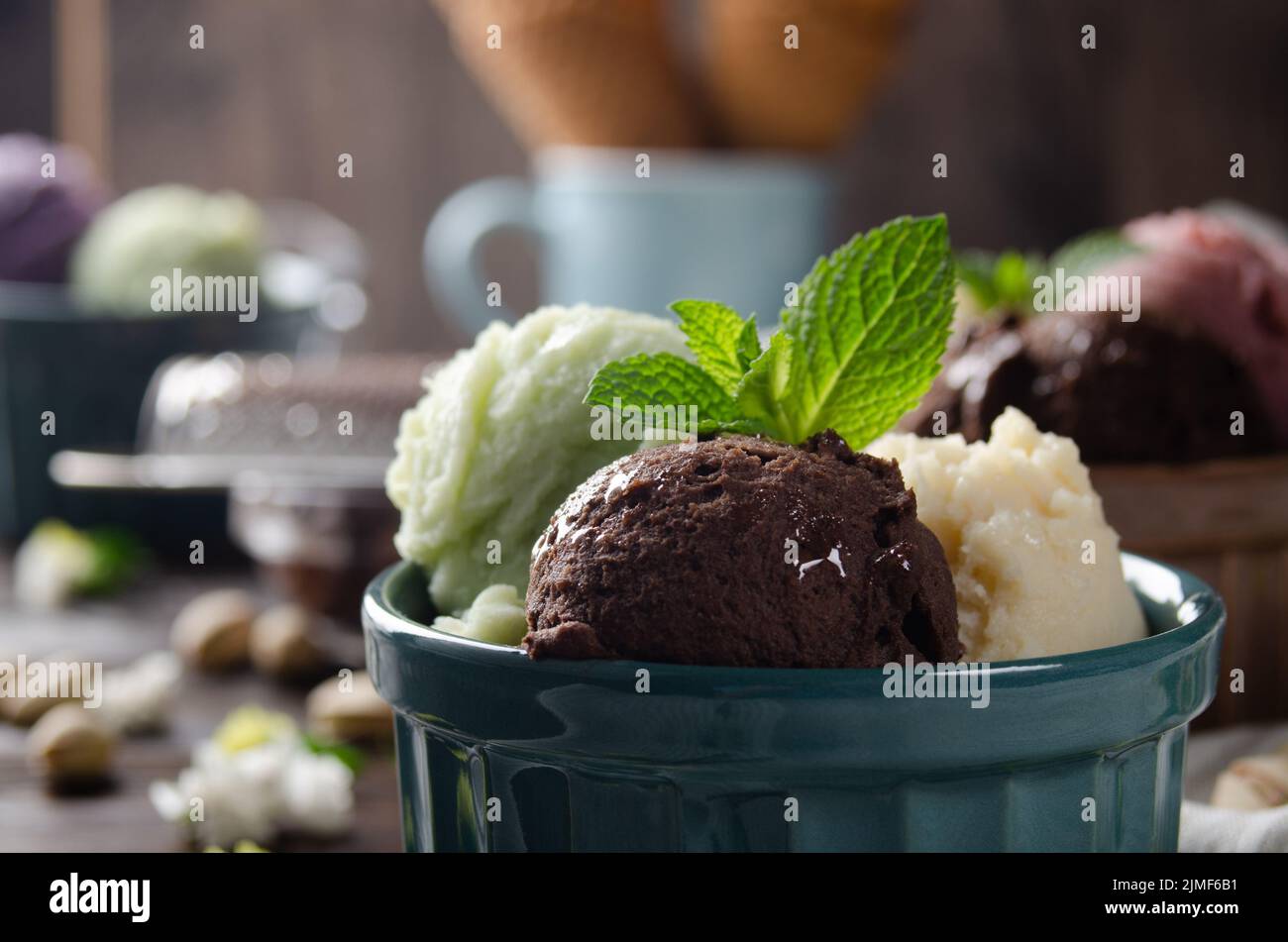 Three scoops of Vanilla pistachio and chocolate icecream balls in clay bowls on wooden kitchen table Stock Photo