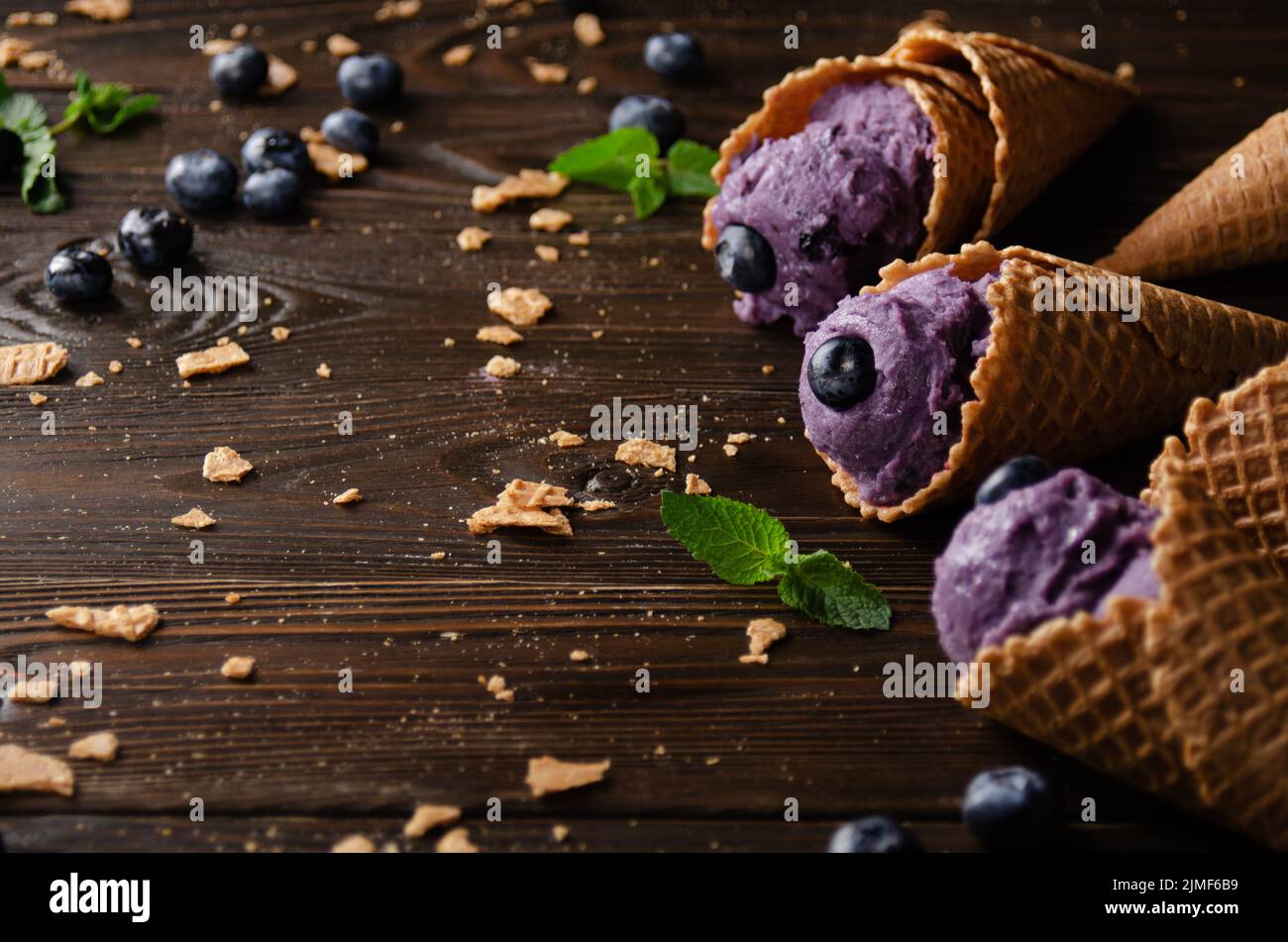 Wafer cones with blackberry icecream on wooden kitchen table with crumbs and berries aside Stock Photo
