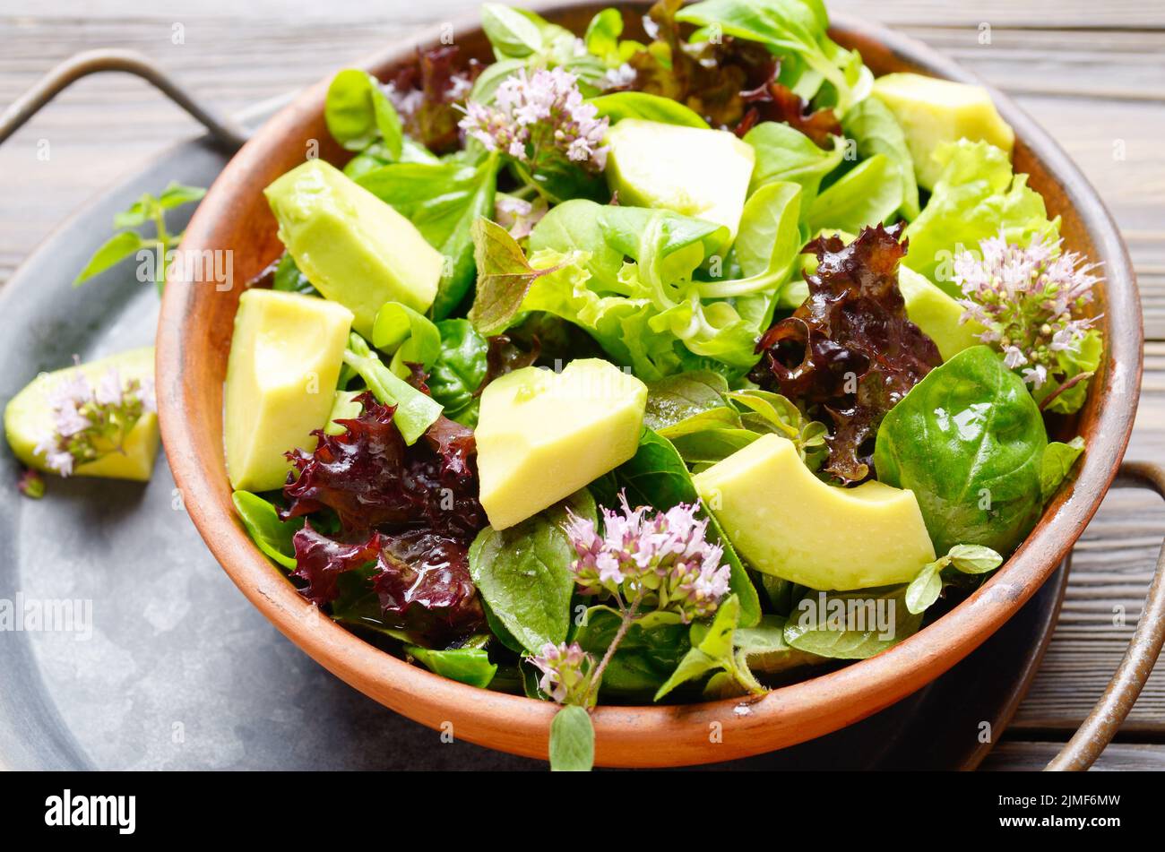 Clay dish with salad of avocado, green and violet lettuce, lamb's lettuce and oregano flowers on vintage metal tray Stock Photo