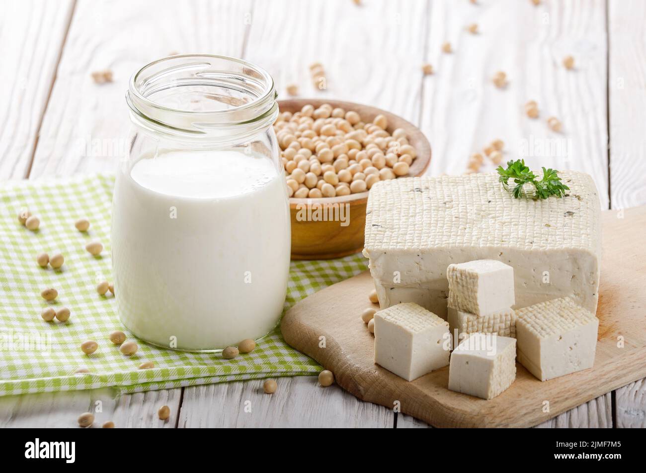 Non-dairy alternatives Soy milk or yogurt in mason jar and tofu on white wooden table with soybeans in bowl aside Stock Photo