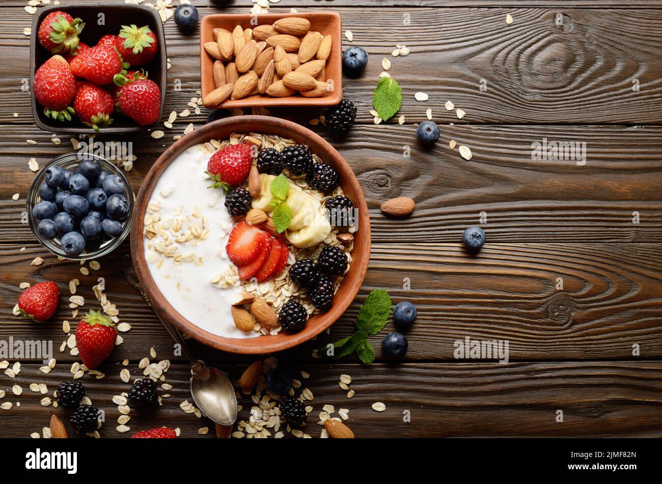 Flat lay top view at Fruit healthy muesli with banana strawberry almonds and blackberry with yogurt  in clay dish on wooden kitc Stock Photo