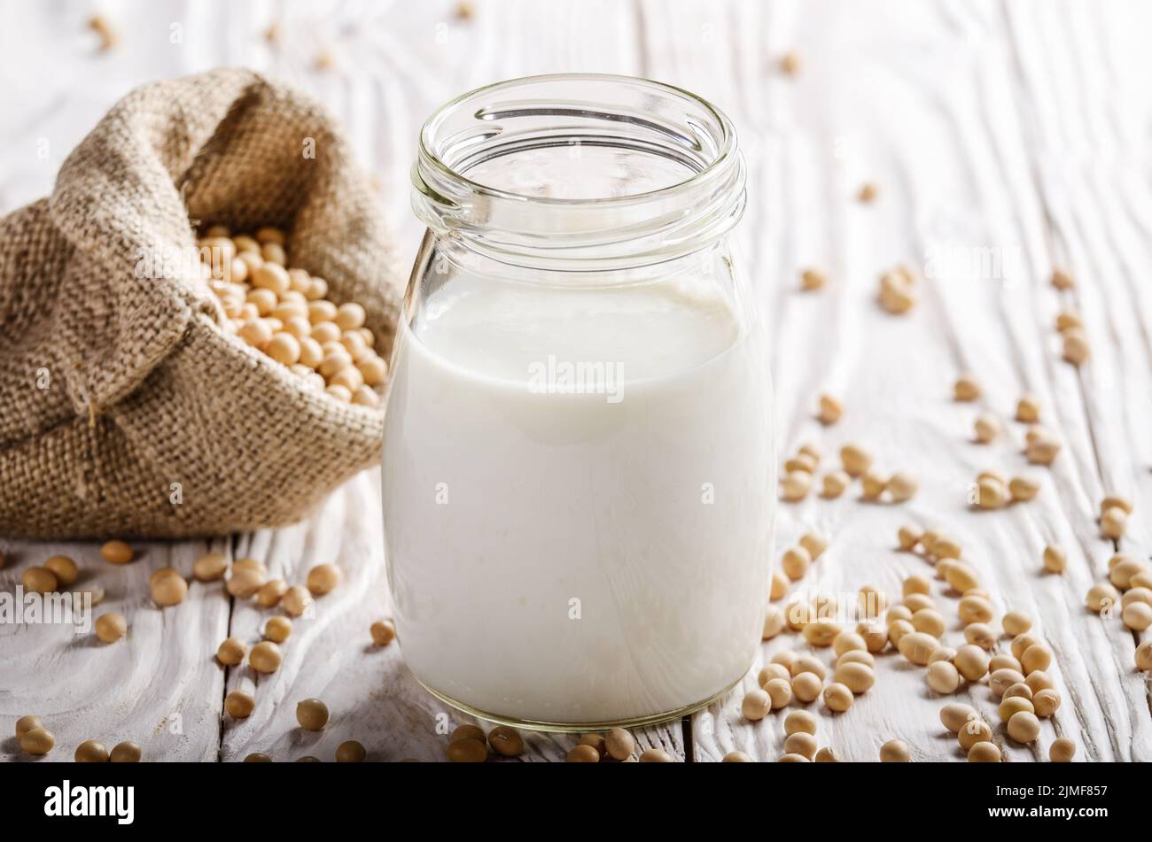Non-dairy alternative Soy milk or yogurt in mason jar on white wooden table with soybeans in hemp sack Stock Photo