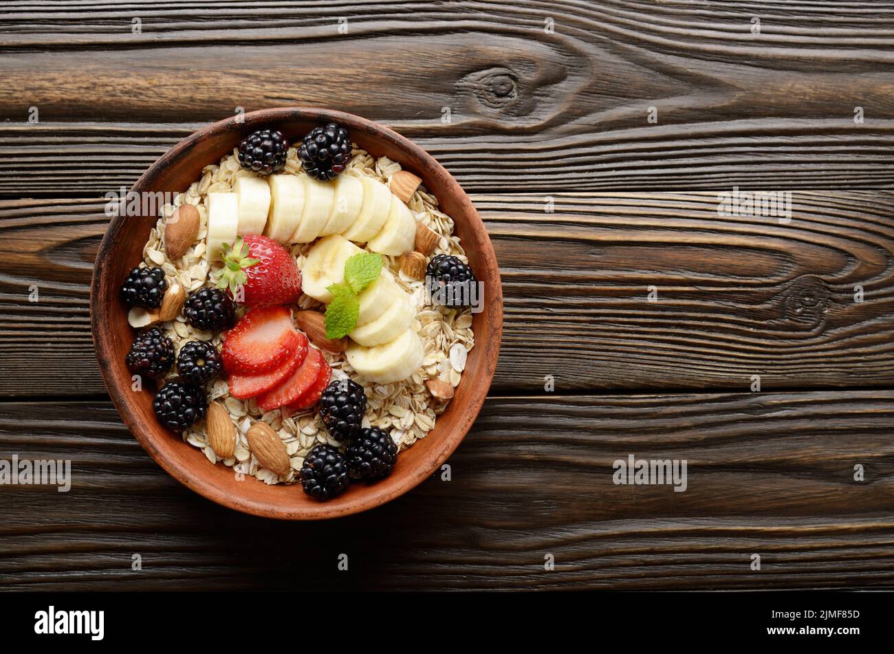 Flat lay top view at Fruit healthy muesli with banana strawberry almonds and blackberry in clay dish on wooden kitchen table Stock Photo