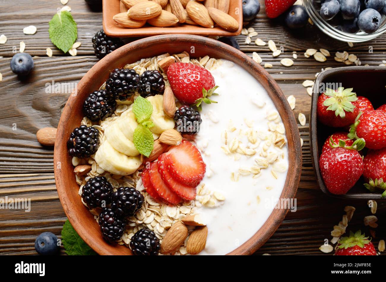 Flat lay top view at Fruit healthy muesli with banana strawberry almonds and blackberry with yogurt  in clay dish on wooden kitc Stock Photo