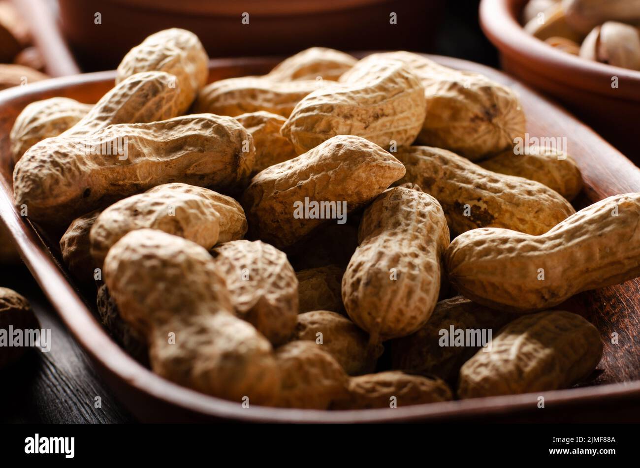 Peanuts in clay bowl on kitchen wooden table food background Stock Photo