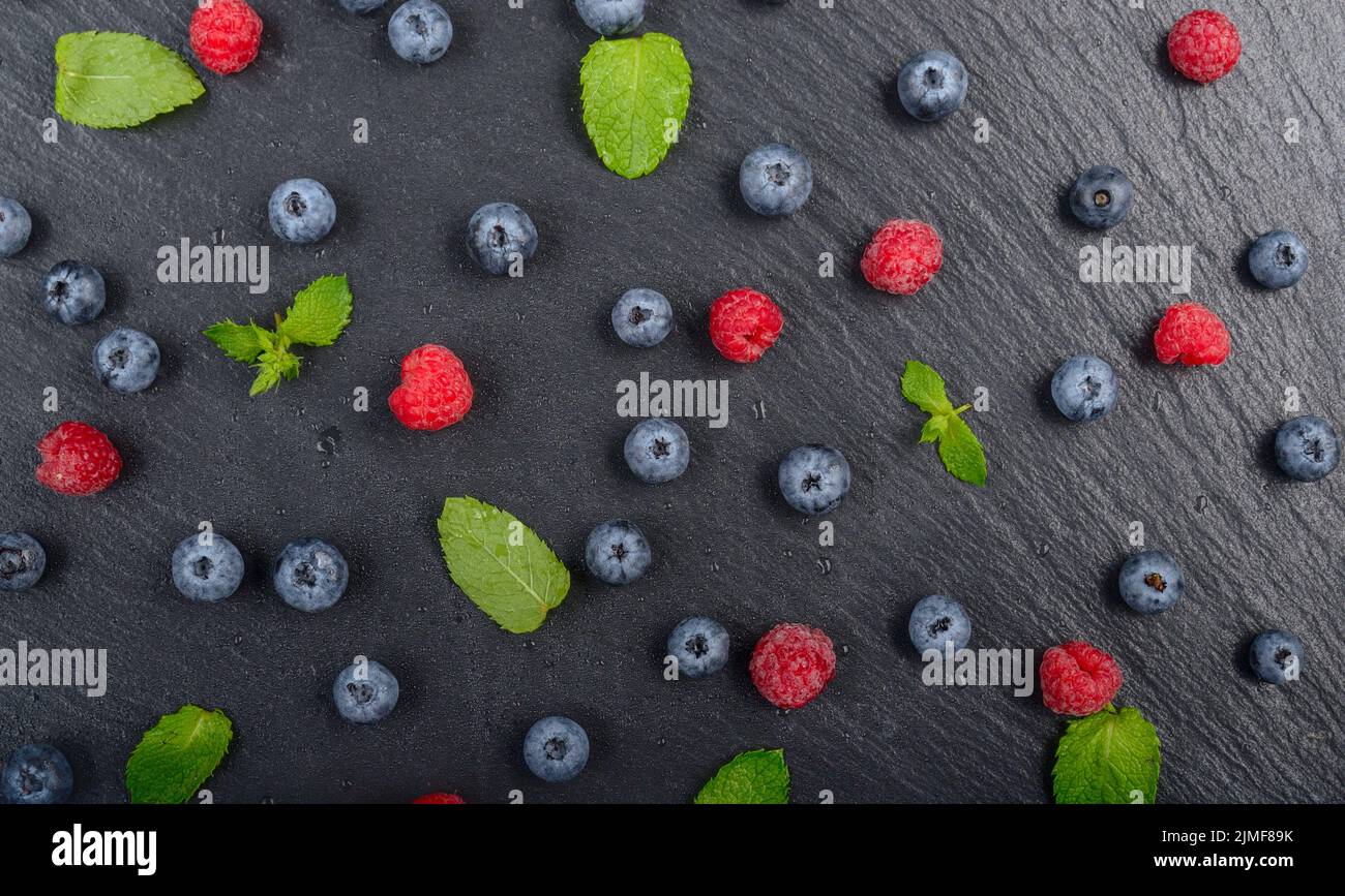 Flat lay view at ripe bilberry and raspberry berries on slate stone tray closeup Stock Photo