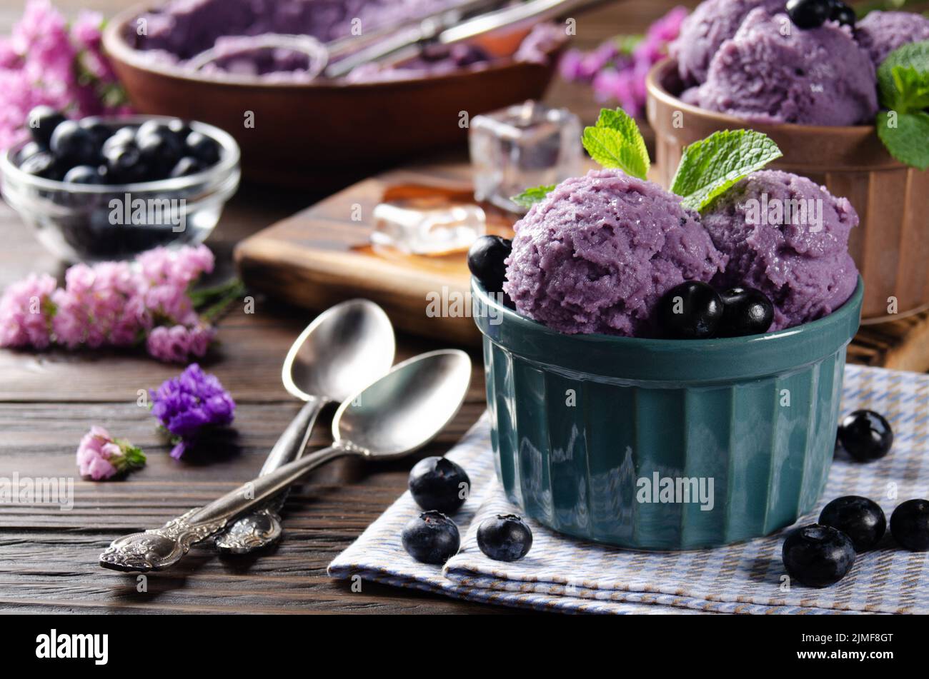 Blackberry icecream balls in clay bowls on wooden kitchen table with flowers and berries aside Stock Photo