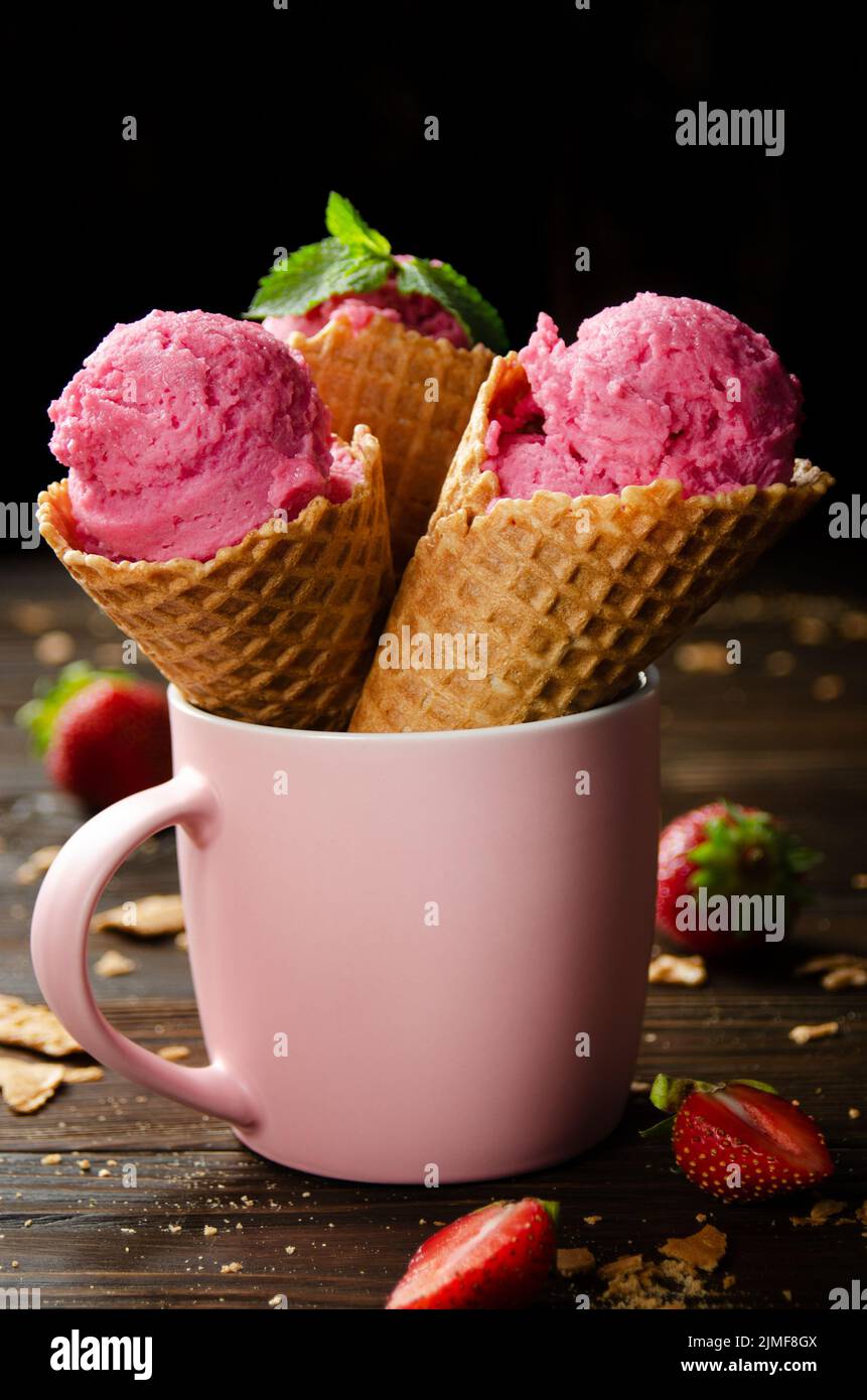 Wafer cones with strawberry icecream in pink mug on wooden kitchen table Stock Photo