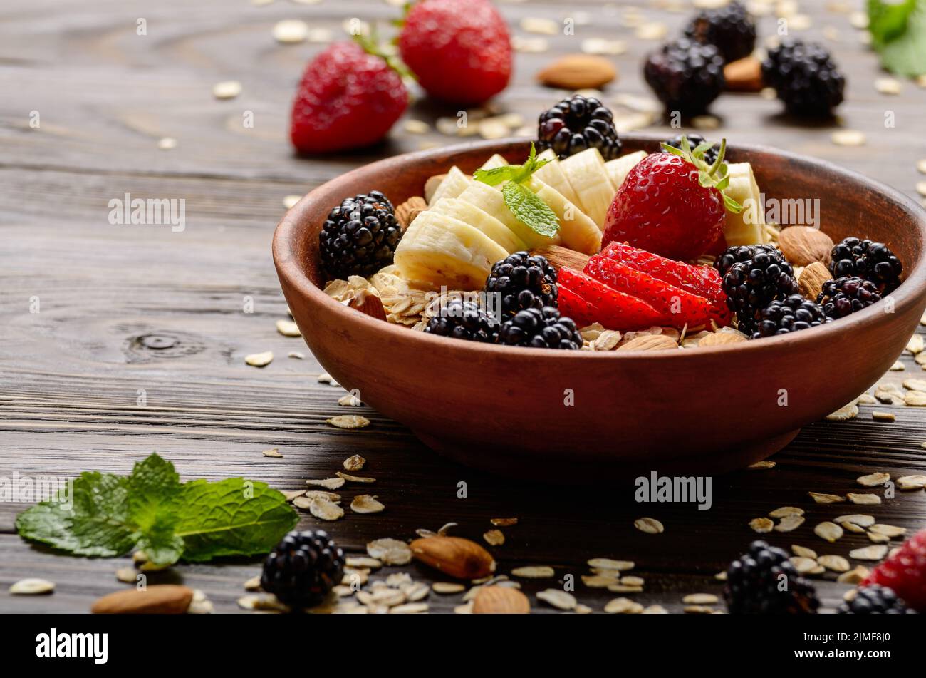 Fruit healthy muesli with banana strawberry almonds and blackberry in clay dish on wooden kitchen table Stock Photo