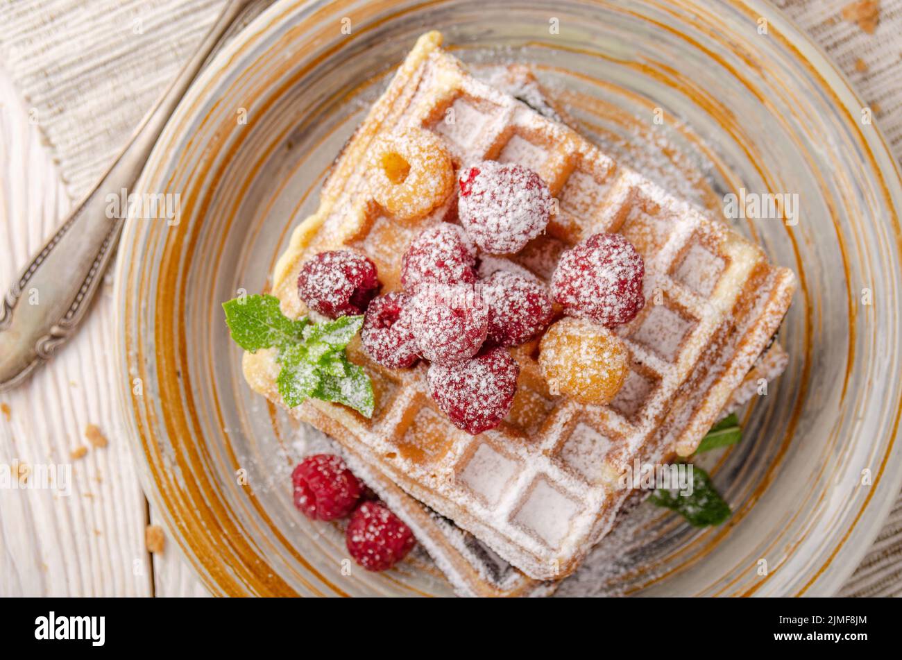 Flat lay view at Belgian waffles served with raspberries and mint leaf dusted with powdered sugar Stock Photo