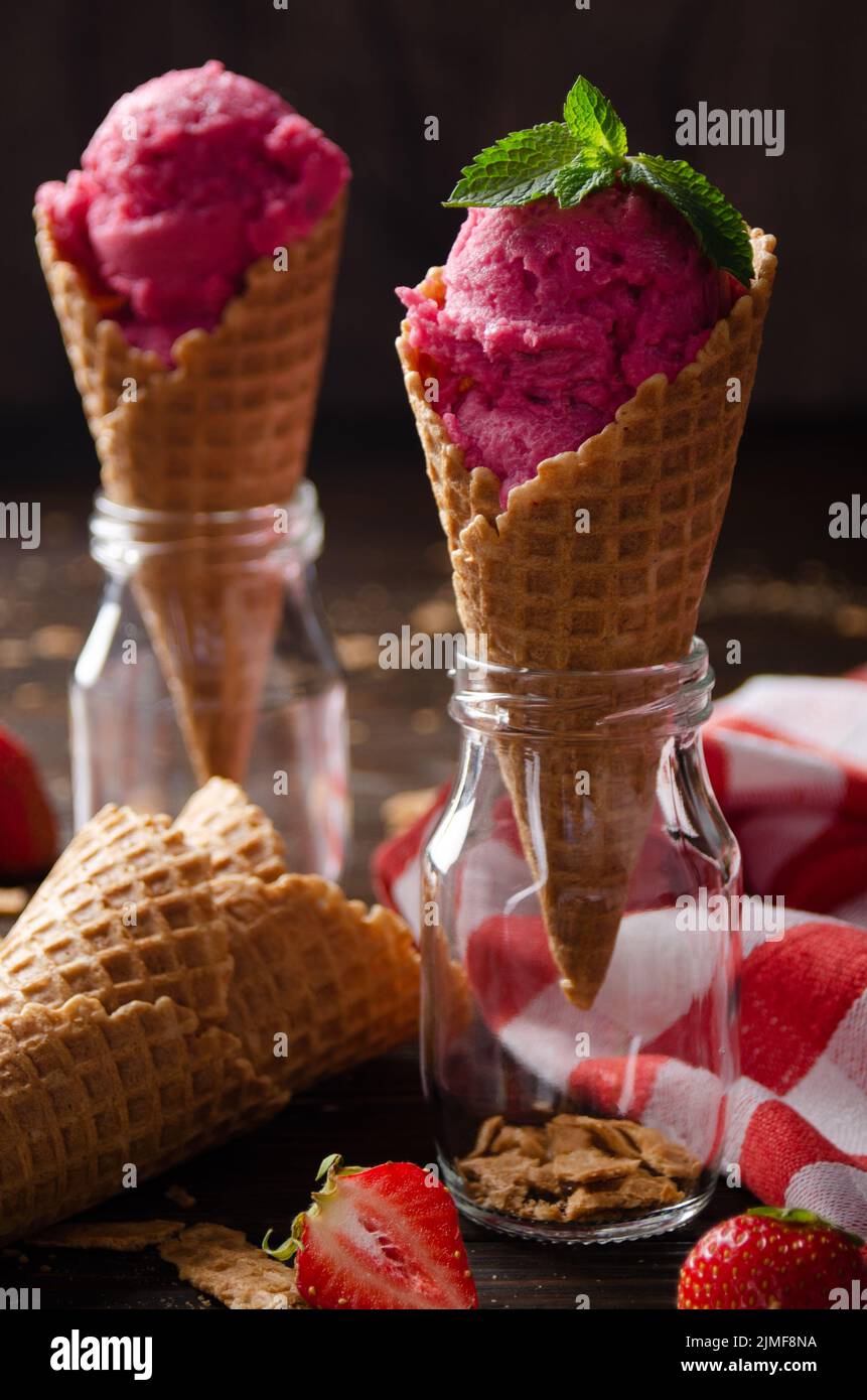 Wafer cones with strawberry icecream in two glass bottles on wooden kitchen table Stock Photo
