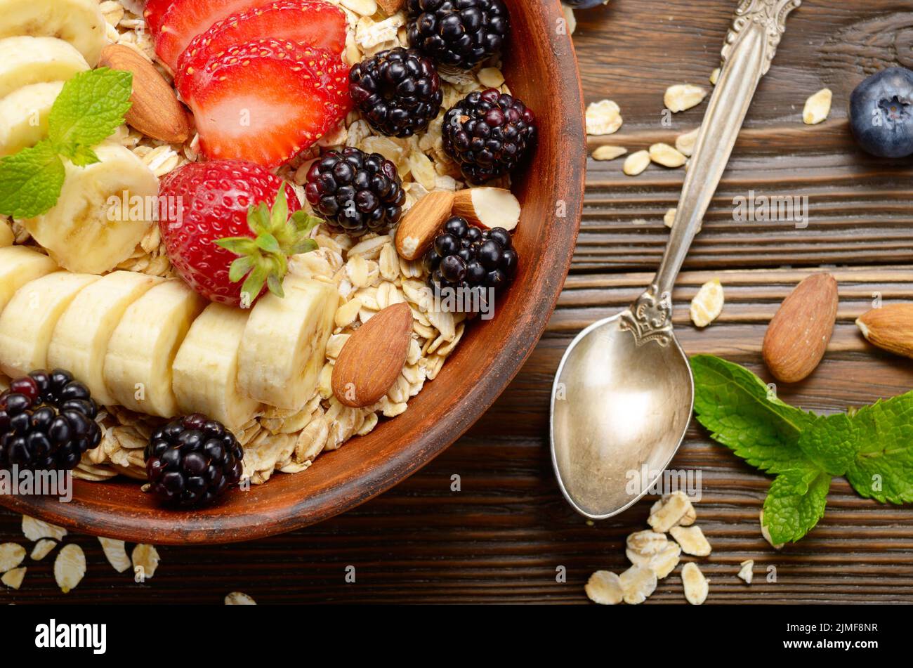 Flat lay top view at Fruit healthy muesli with banana strawberry almonds and blackberry in clay dish on wooden kitchen table Stock Photo