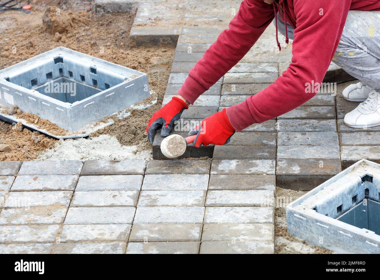 Paving slabs. A worker in red gloves is laying paving slabs around storm sewer hatches with a rubber mallet. Copy space. Stock Photo