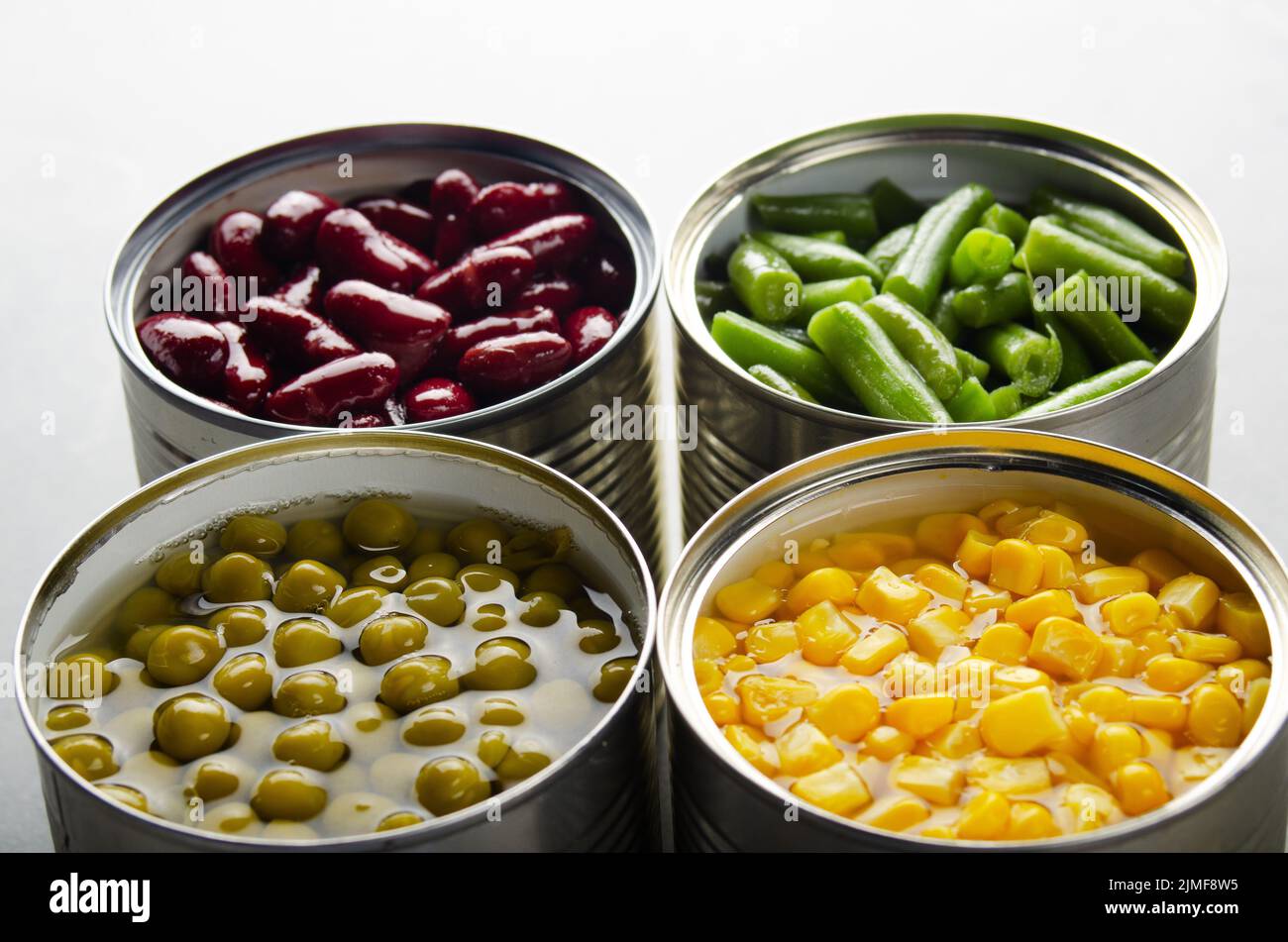 Canned kidney beans, green beans, peas and corn in opened tin cans on kitchen table. Non-perishable foods background Stock Photo