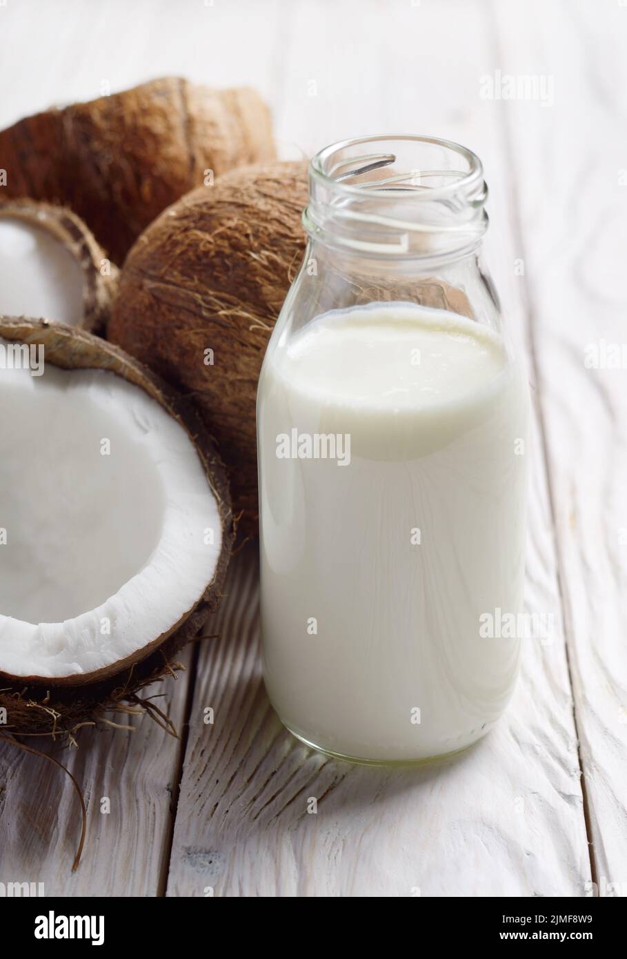 Glass bottle with milk or yogurt on white wooden kitchen table with coconut aside Stock Photo