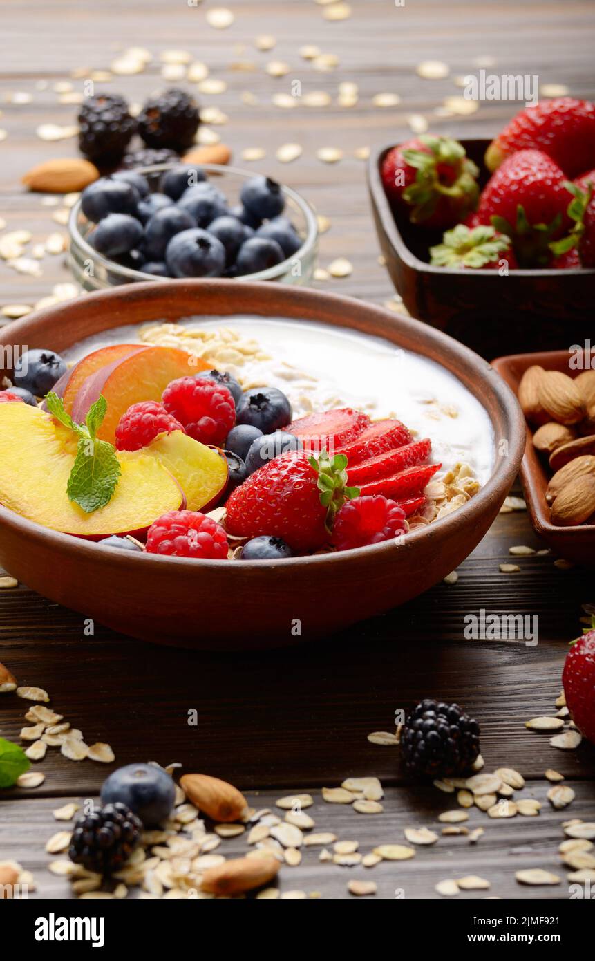 Fruit healthy muesli with peaches strawberry almonds and blackberry in clay dish with yogurt on wooden kitchen table Stock Photo