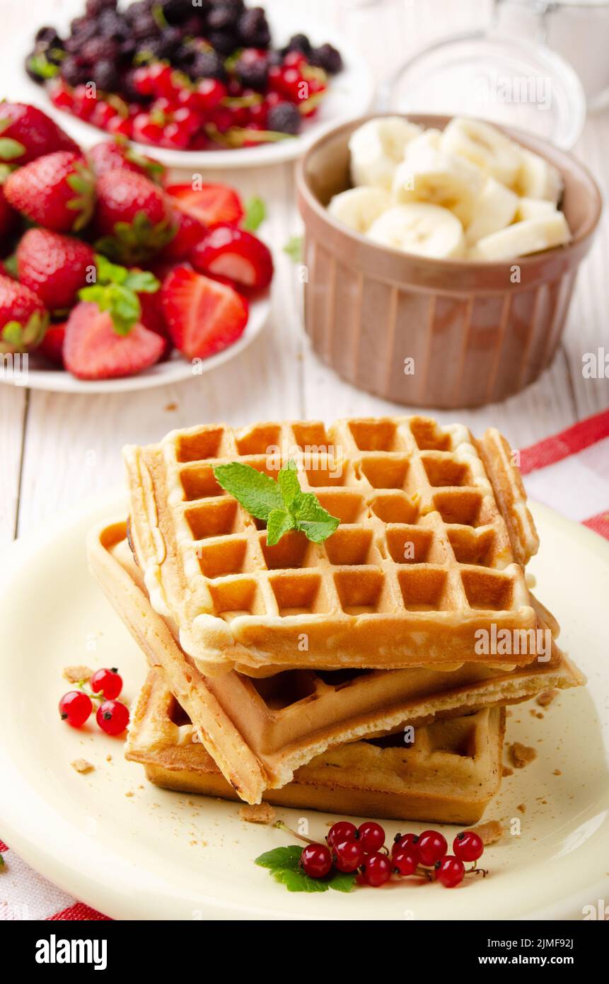 Stack of three belgian waffles on white kitchen table with strawberries bananas and red currant Stock Photo