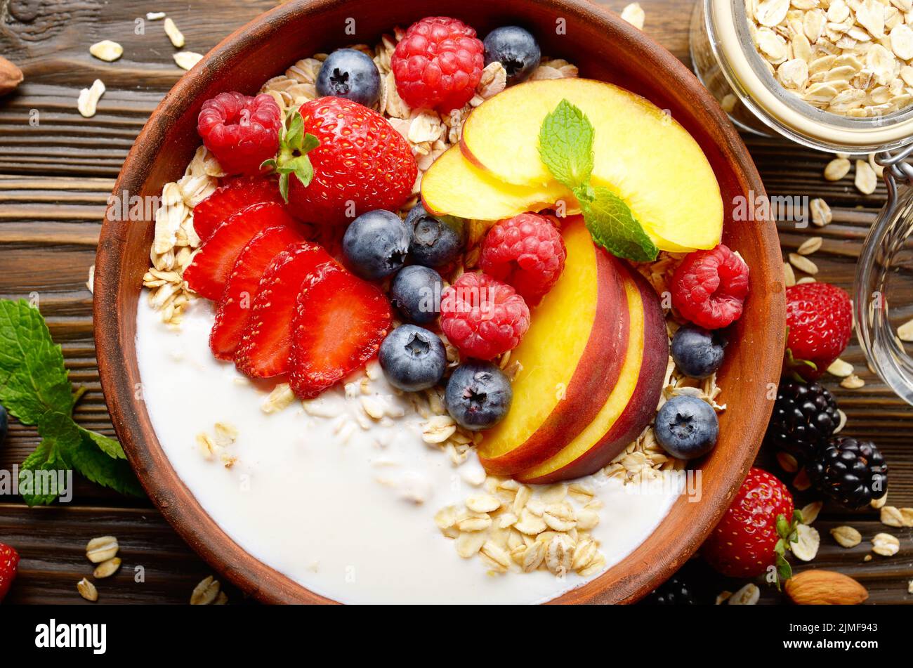 Flat lay of fruit healthy muesli with peaches strawberry almonds and blackberry in clay dish with yogurt Stock Photo