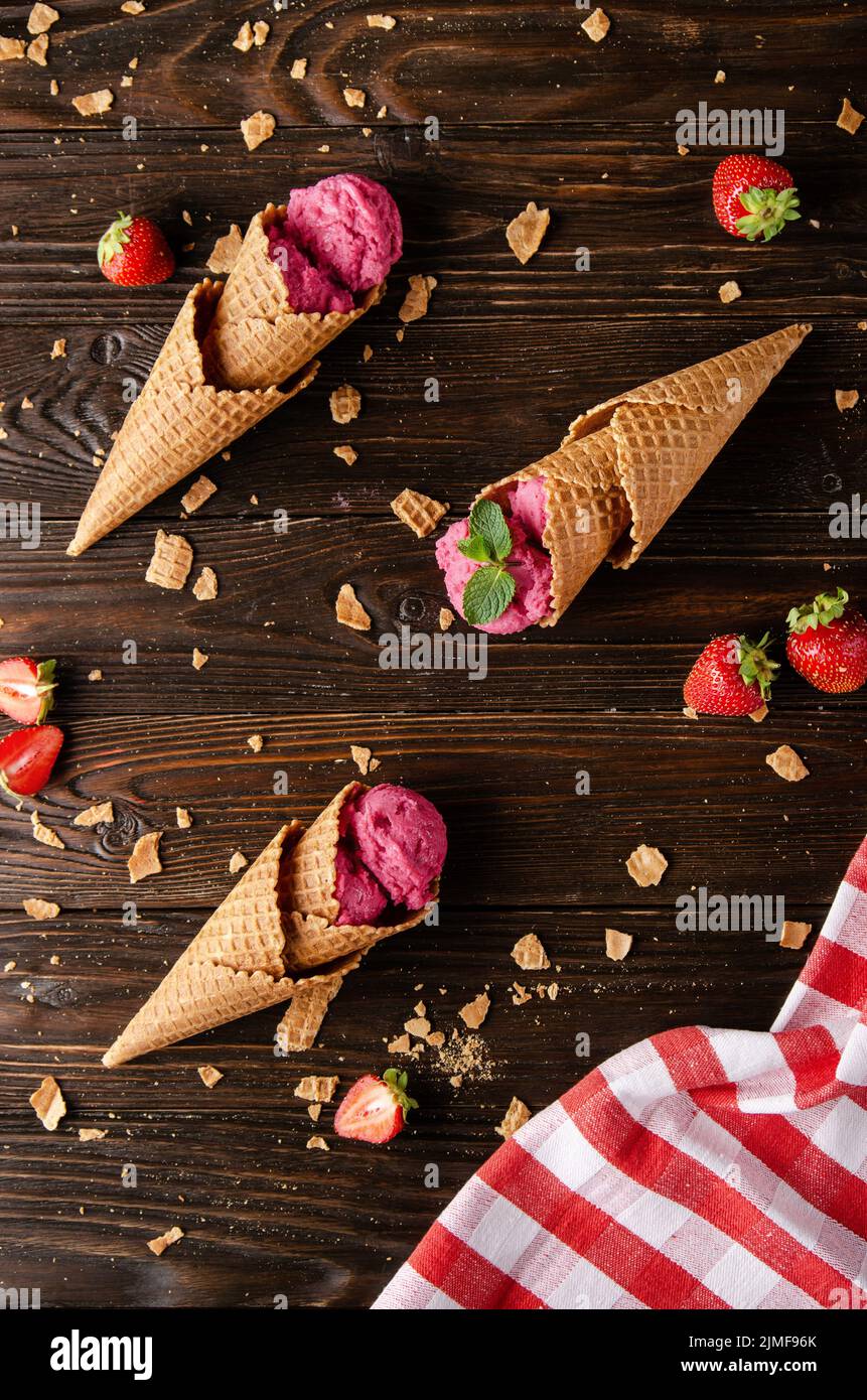 Wafer cones with strawberry icecream on wooden kitchen table with crumbs and berries aside Stock Photo
