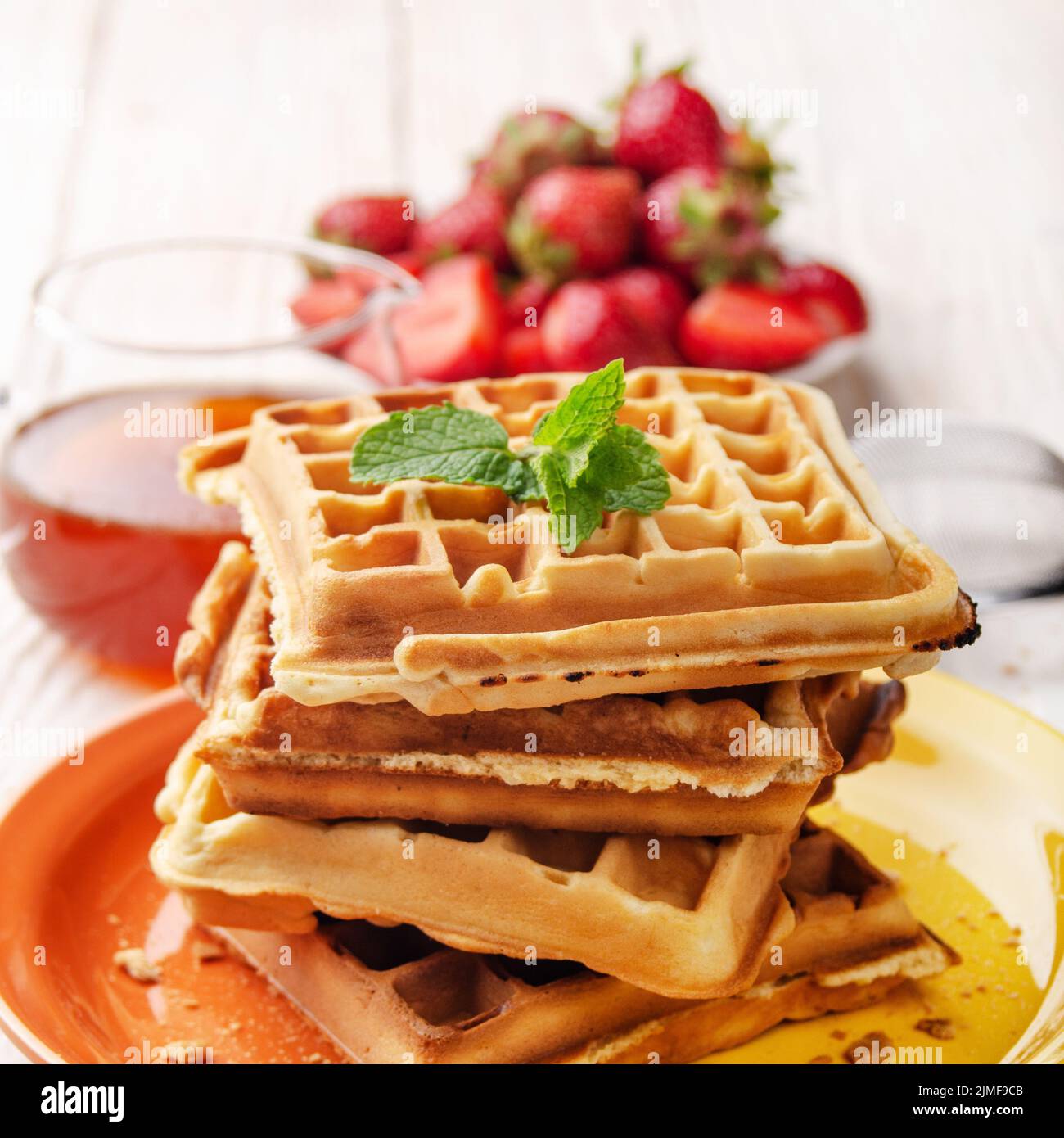 Pile of belgian waffles on white wooden kitchen table with strawberries and syrup aside Stock Photo