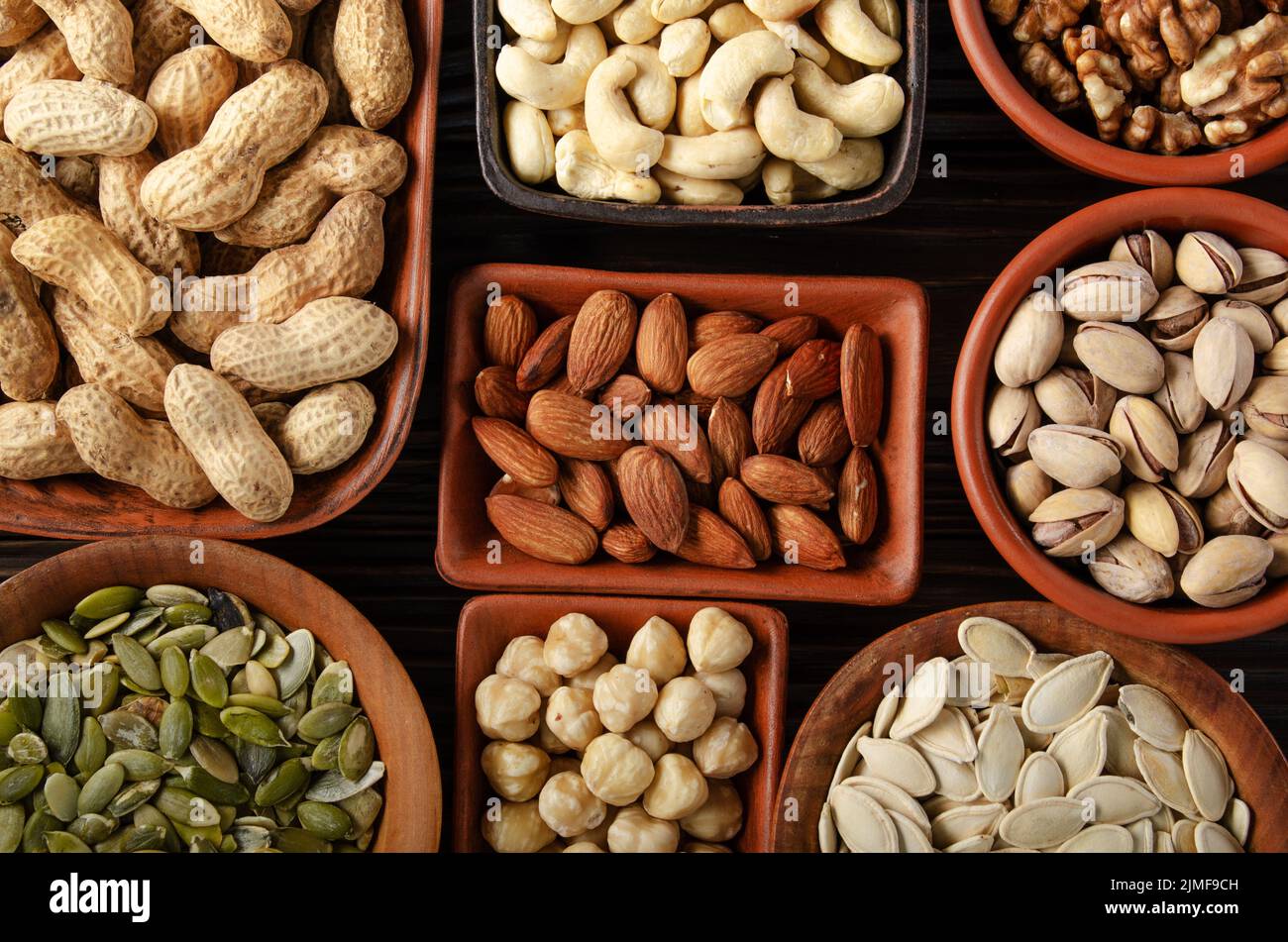 Flat lay view at assorted nuts and seeds in clay bowls on wooden kitchen table Stock Photo