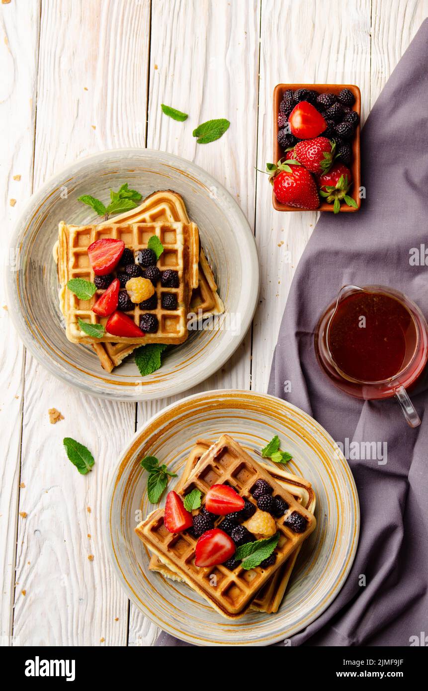 Flat view at belgian waffles served with strawberries and blackberries on white wooden kitchen table closeup Stock Photo