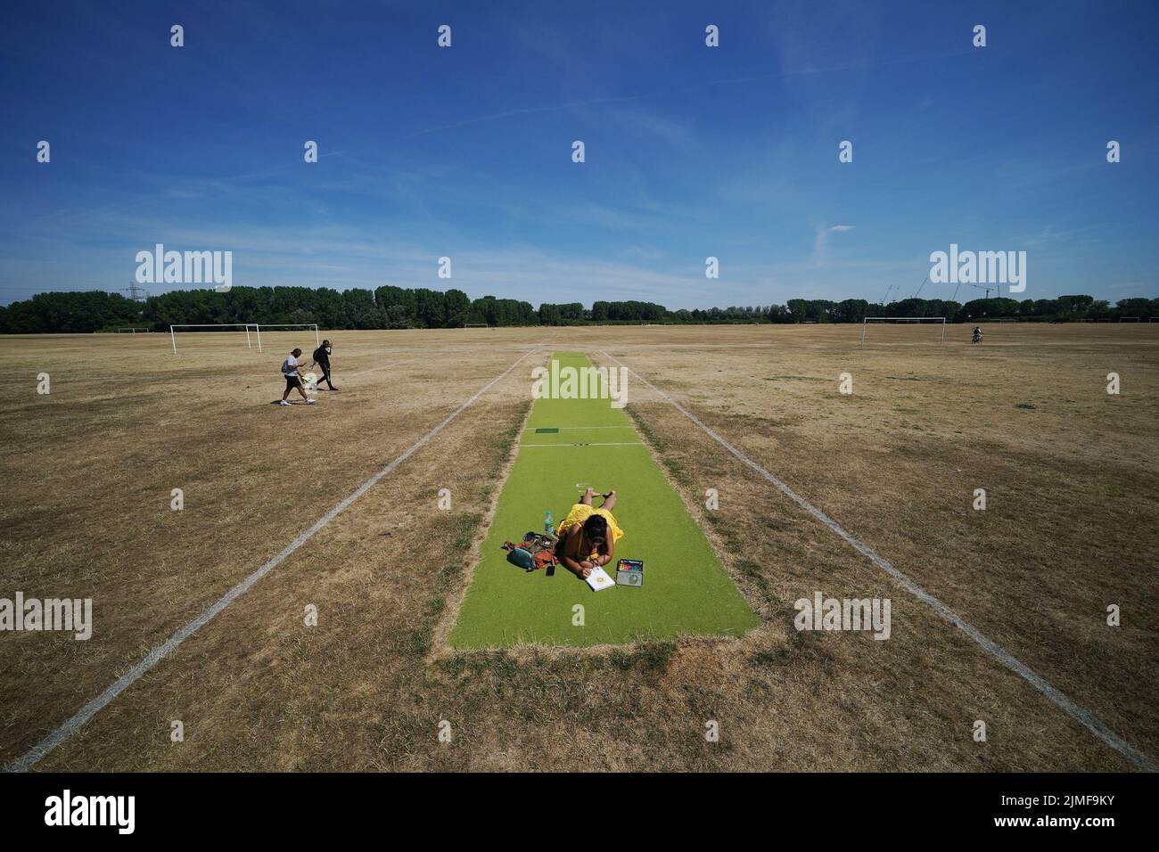 A woman relaxes on a green cricket pitch surrounded by parched football pitches, on Hackney Marshes, east London. Picture date: Saturday August 6, 2022. Stock Photo