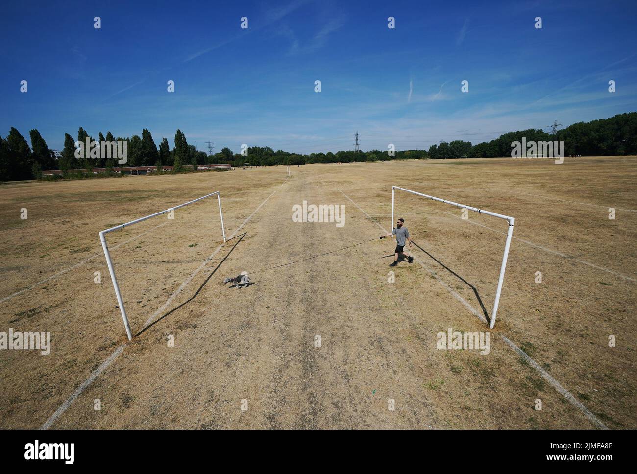 Jake Rees walking his dog Pluto, a two-and-a- half years old Bedlington terrier, on the parched football pitches of Hackney Marshes, east London. Picture date: Saturday August 6, 2022. Stock Photo
