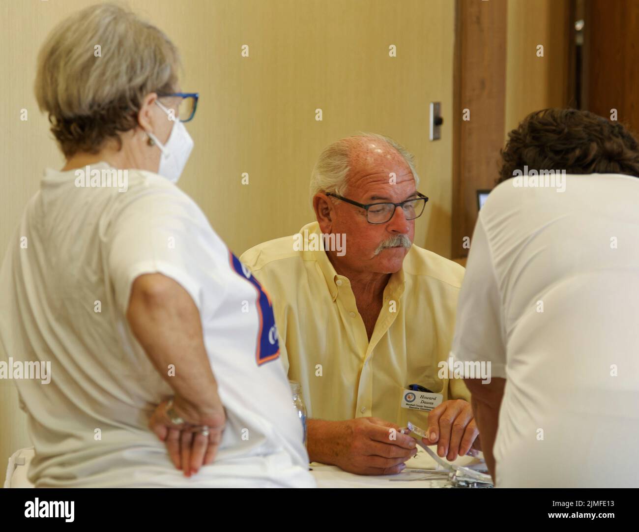 Calvert City, KY, USA. 05 Aug 2022. A masked attendee watches as Marshall County Democratic Party Executive Committee member Howard Dawes (center) checks in another attendee at the 25th Mike Miller Memorial Marshall County Bean Dinner at Kentucky Dam Village State Resort Park. A spokeswoman said 167 guests preregistered for the event and organizers expected approximately 200 people to attend. (Credit: Billy Suratt/Apex MediaWire via Alamy Live News) Stock Photo