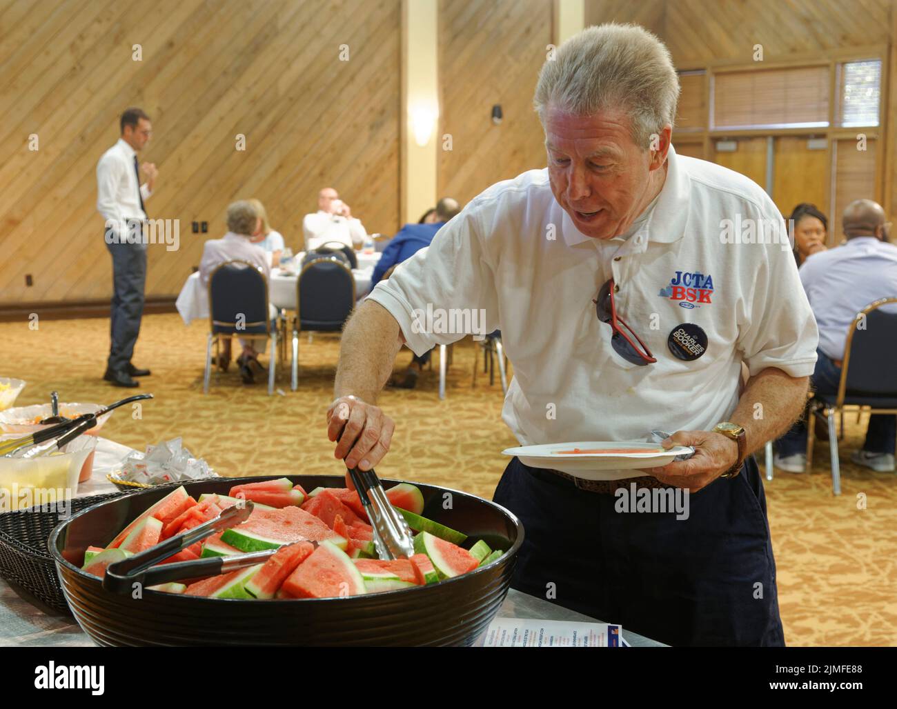 Calvert City, KY, USA. 05 Aug 2022. An unidentified attendee helps himself to sliced watermelon in the buffet line as Marshall County Democratic Party Executive Committee Chair Drew Williams (back left) talks with guests at the 25th Mike Miller Memorial Marshall County Bean Dinner at Kentucky Dam Village State Resort Park. The Marshall County Democratic Party fundraiser is held the night before the annual St. Jerome Fancy Farm Picnic, the traditional start of political campaign season in Kentucky. (Credit: Billy Suratt/Apex MediaWire via Alamy Live News) Stock Photo