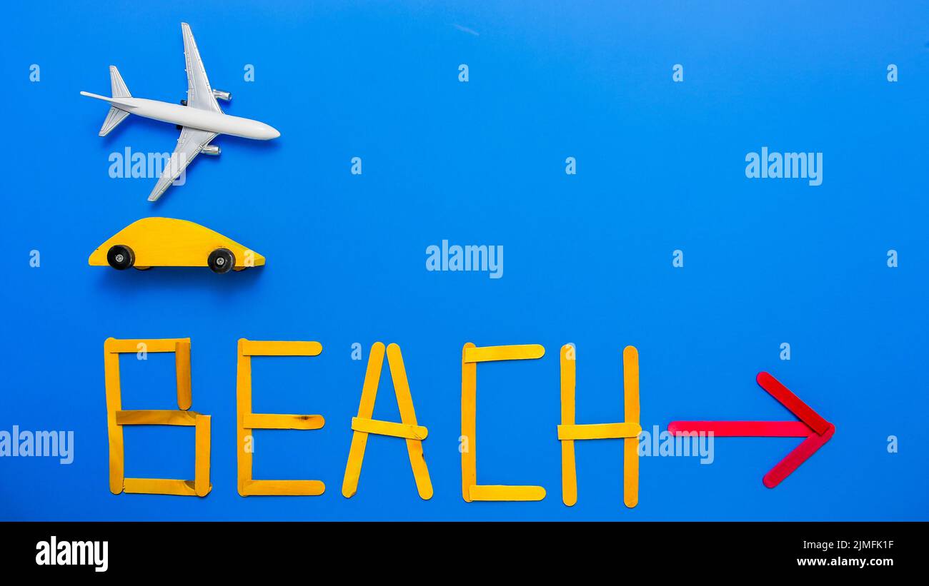 Blue background with toy airplane, yellow wooden car and text beach with red arrow from above Stock Photo
