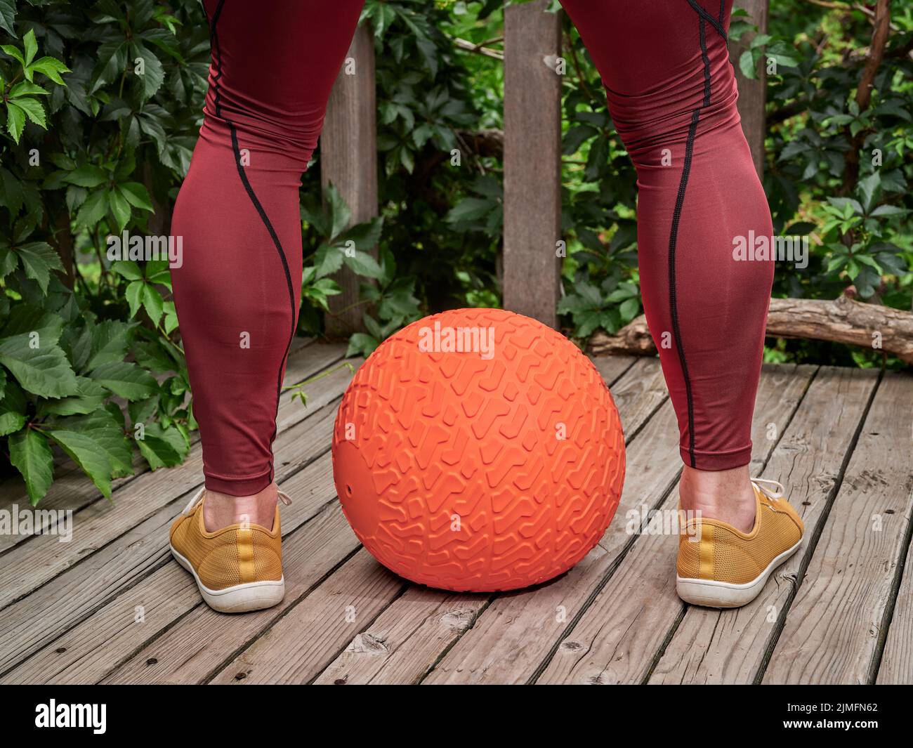 male in compression pants is exercising with a heavy slam ball on a backyard deck, functional fitness and backyard gym concept Stock Photo