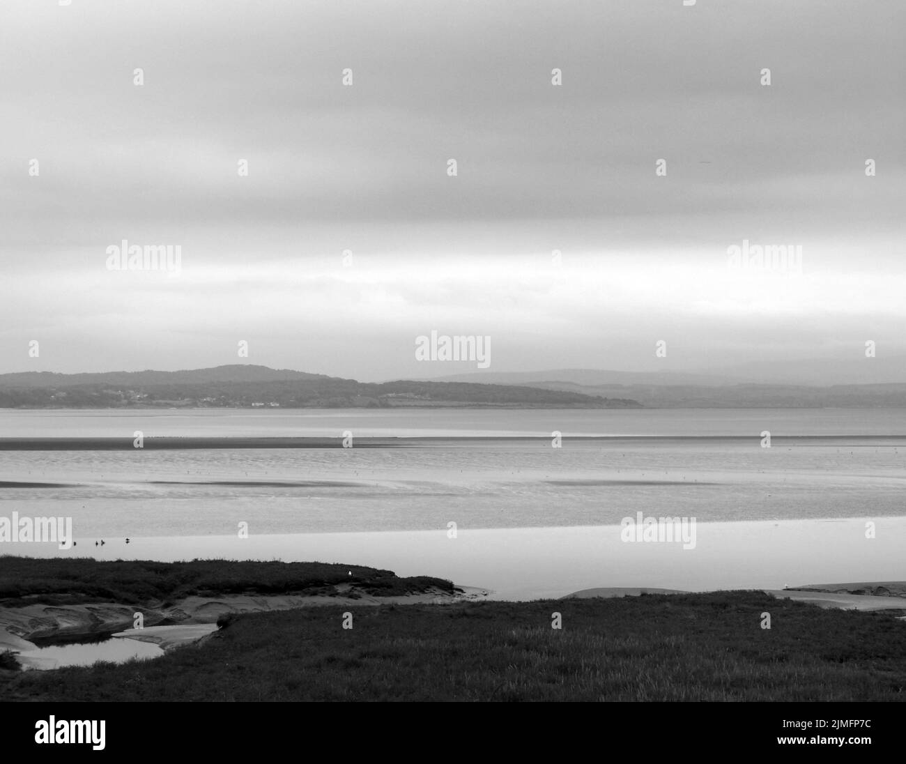 Monochrome atmospheric view of the coast at grange over sands in cumbria with grass covered wetland in the foreground and the no Stock Photo