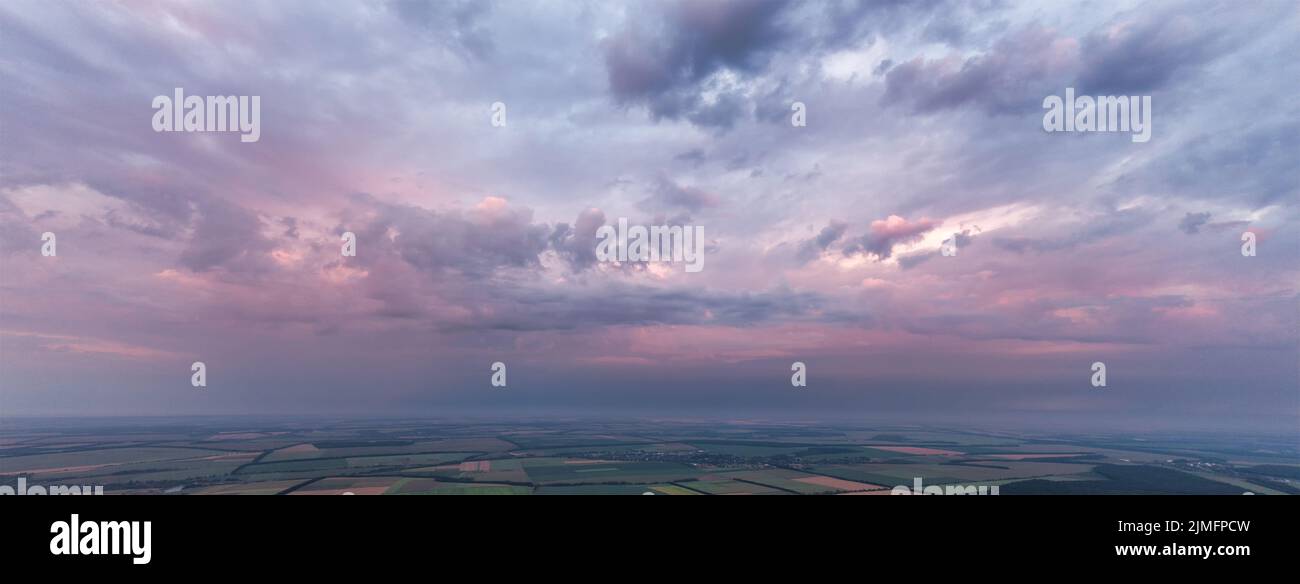 Panorama of pink sky with clouds over green land and fields. Stock Photo