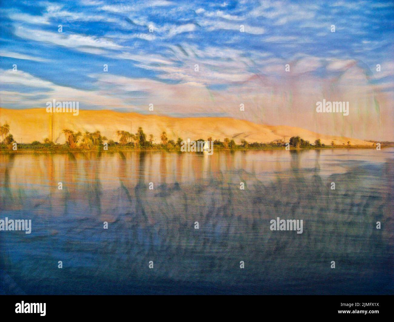 Along the Nile River in Egypt, with blue water, blue sky, and the bright white sail of a small boat. With a thin strip of greenery and dunes behind th Stock Photo