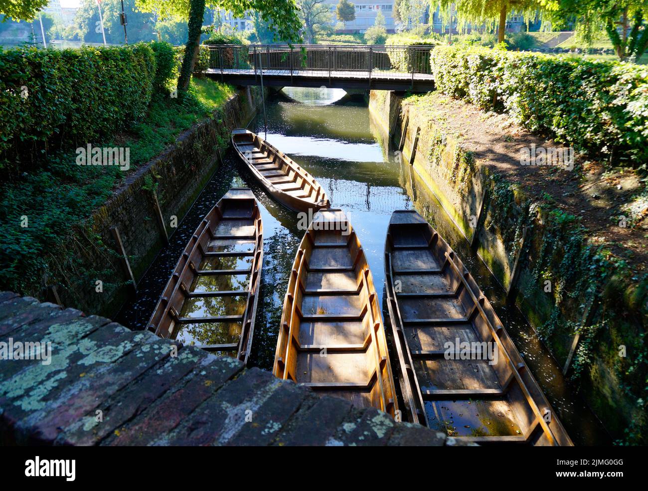 a scenic view of a little bridge, wooden boats (Ulmer Schachteln) underneath it, green trees and the old town wall in the city of Ulm in Germany Stock Photo