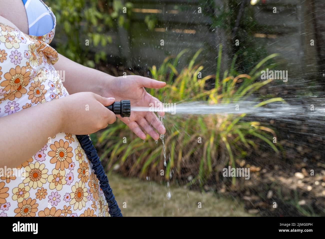 Young Woman waters garden with a hosepipe before the hosepipe ban comes