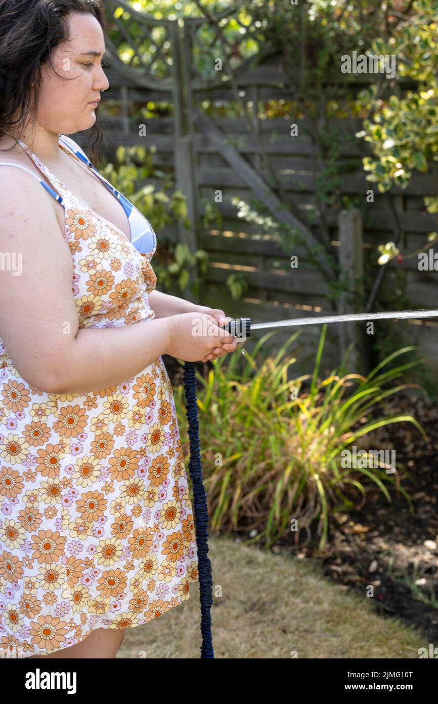Young Woman waters garden with a hosepipe before the hosepipe ban comes
