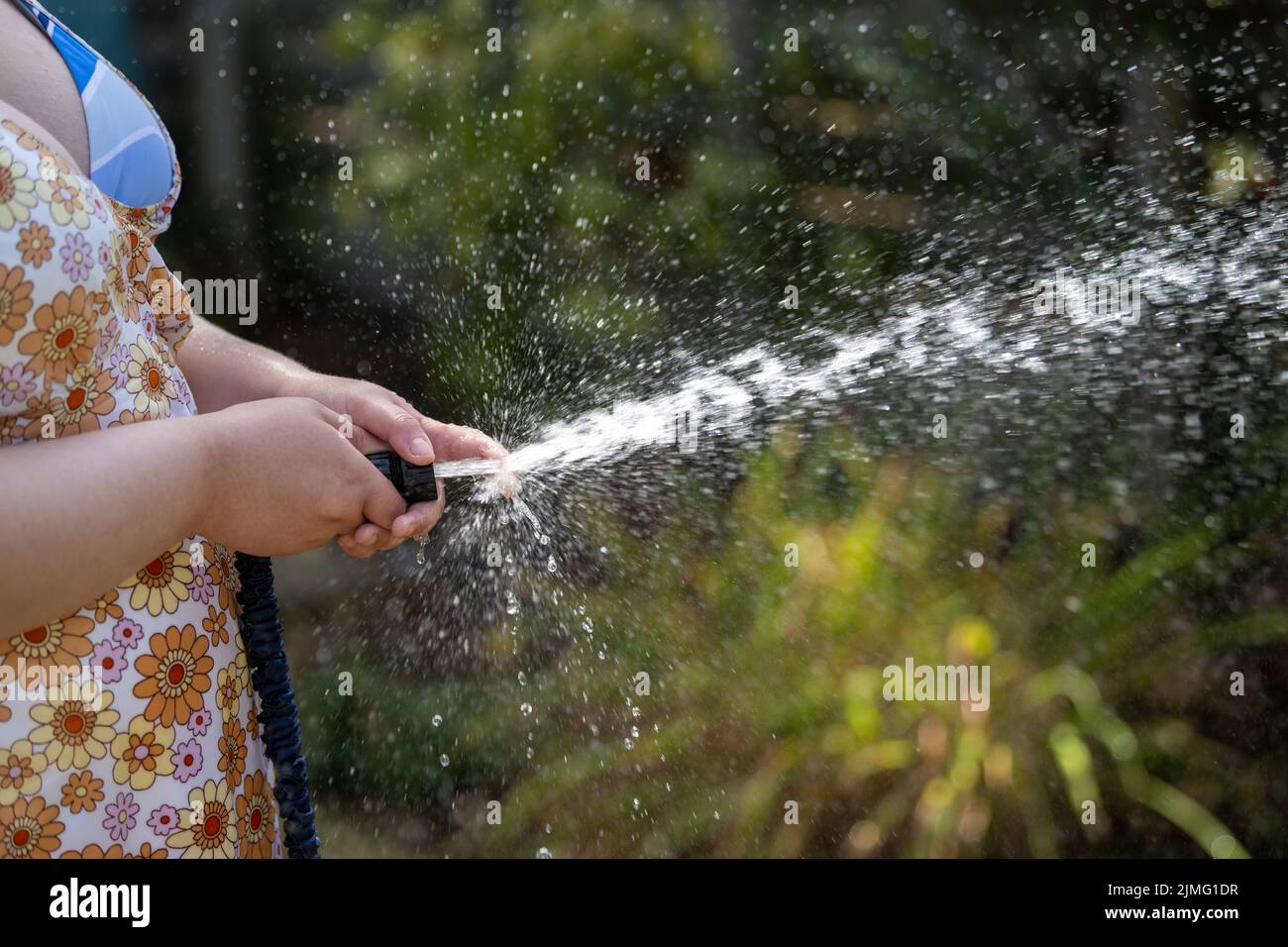 Young Woman waters garden with a hosepipe before the hosepipe ban comes