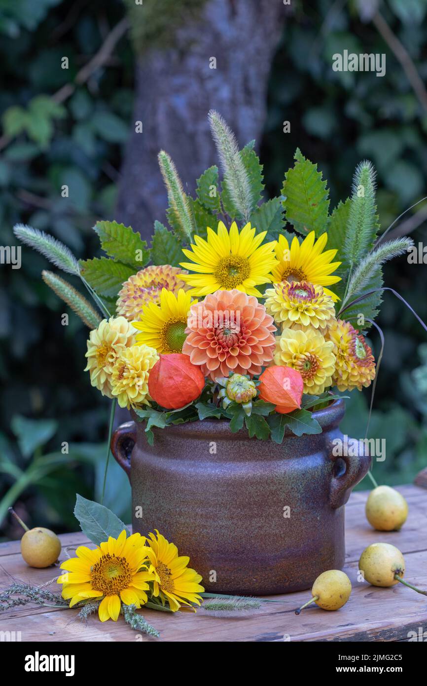 bouquet of orange and yellow dahlias and sunflowers in old clay pot Stock Photo
