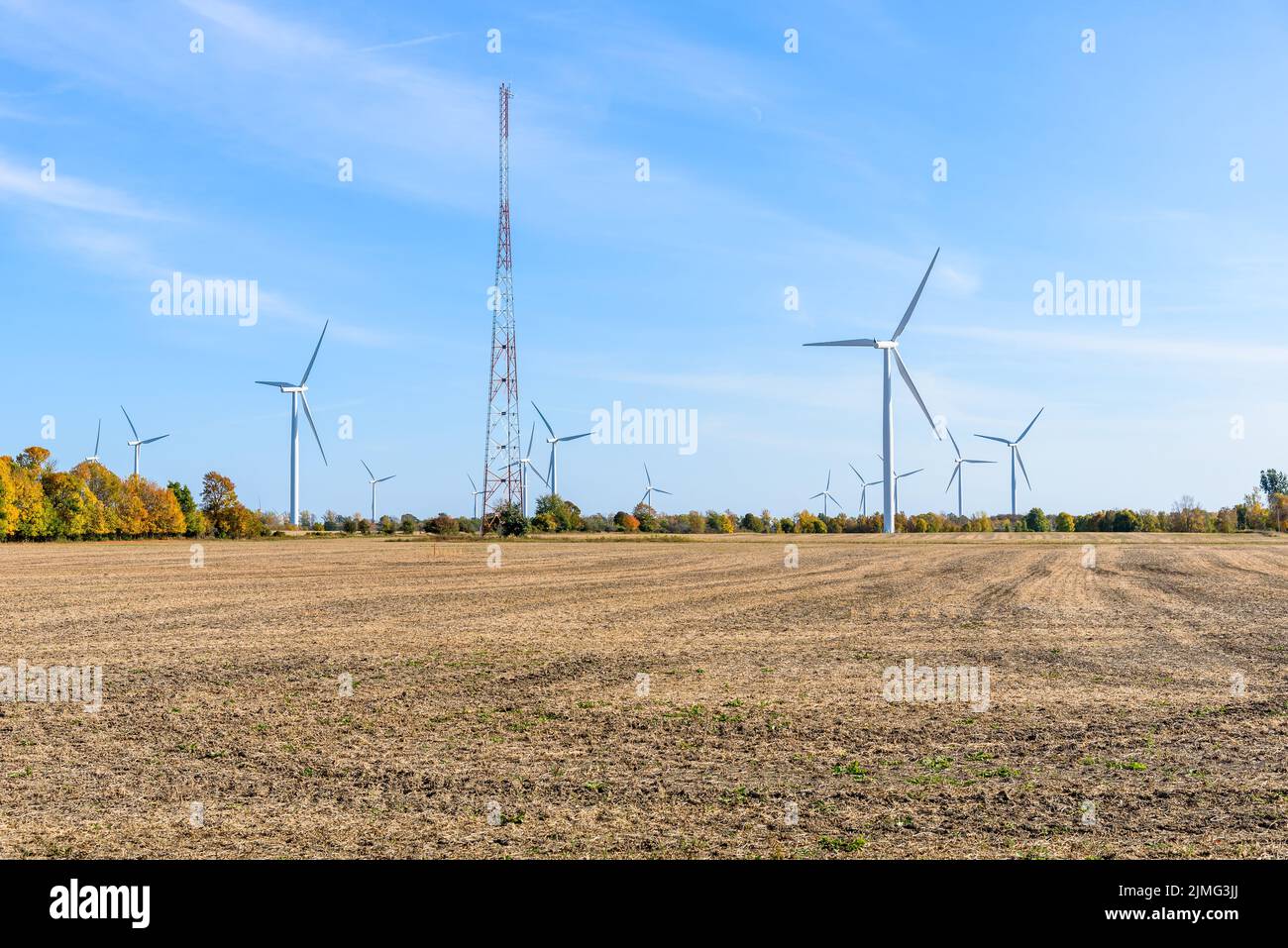 Wind turbines and tall antenna in a harvested field under blue sky in autumn Stock Photo