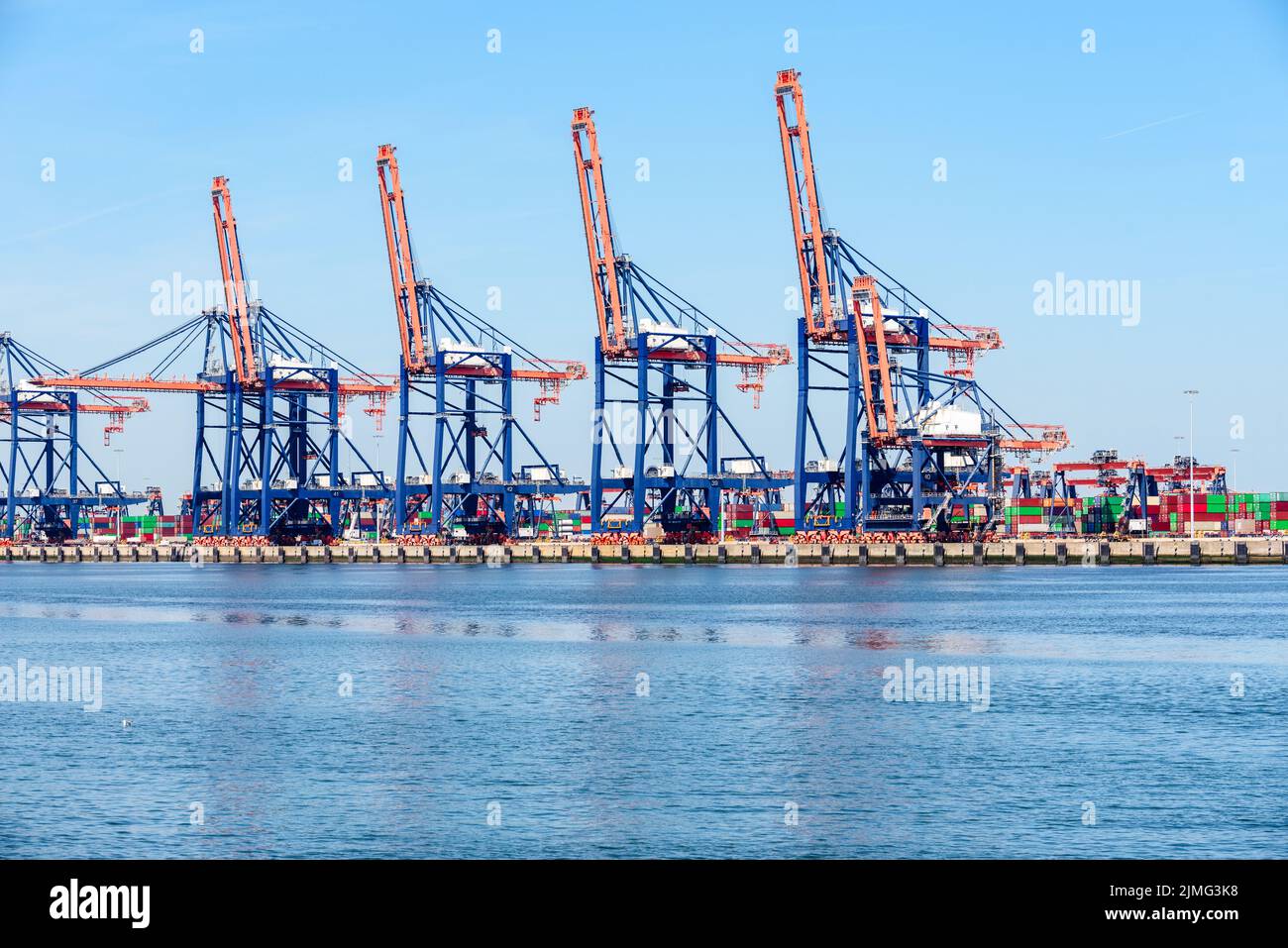 Tall gantry cranes on a commercial dock on a sunny summer day. Stacks of colourful containers are visible in background. Stock Photo