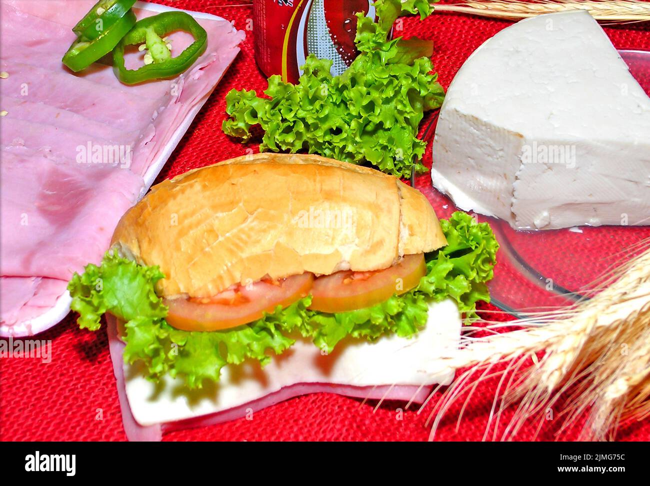 Table decorated with branches of wheat. Sandwich of salt bread stuffed with tomato, lettuce, ham and cheese. Stock Photo